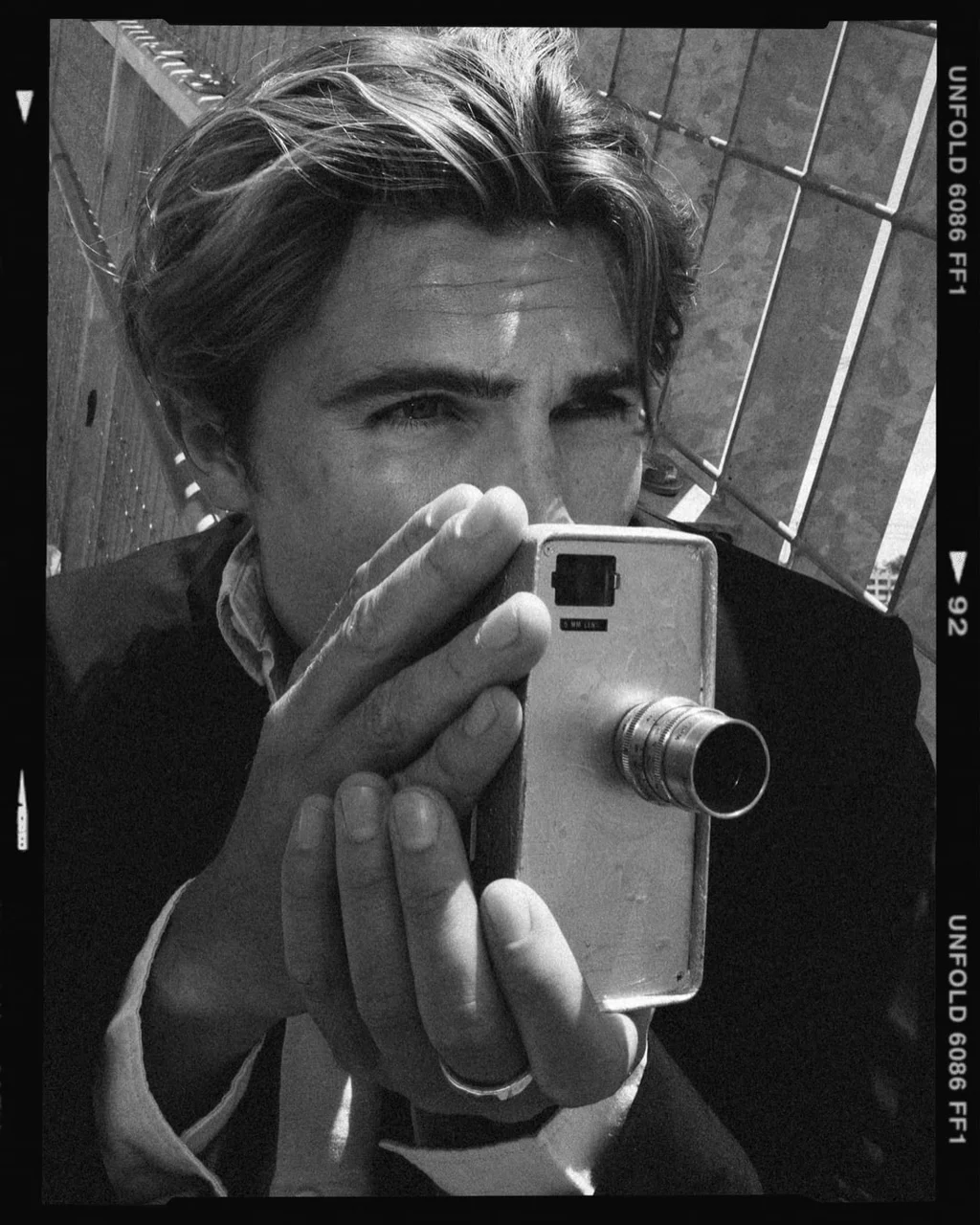Black-and-white portrait holding a vintage camera beside a metal railing