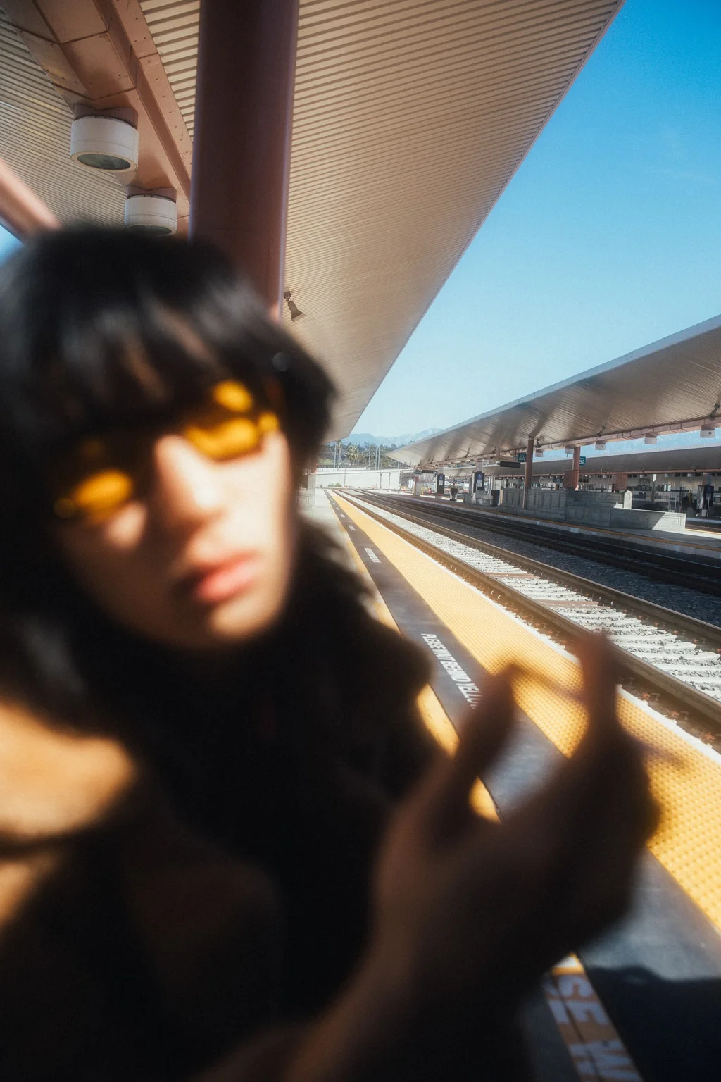 Blurred portrait in amber sunglasses beside a train platform