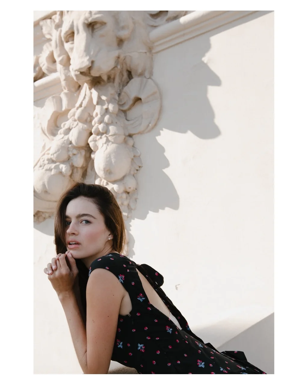 Portrait in a floral dress beneath a carved stone face
