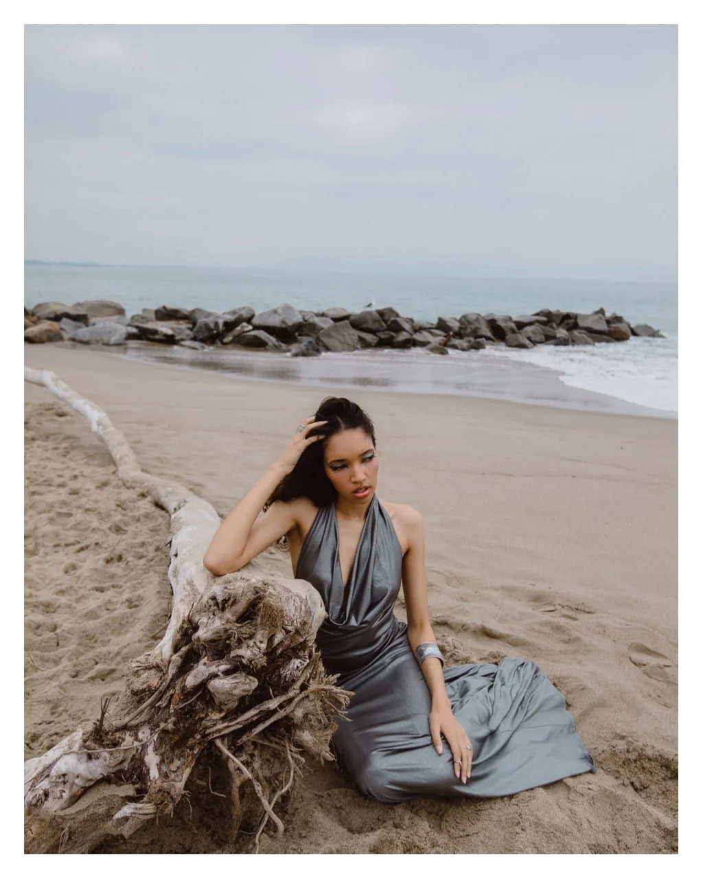 Figure in a silver dress beside driftwood on the beach