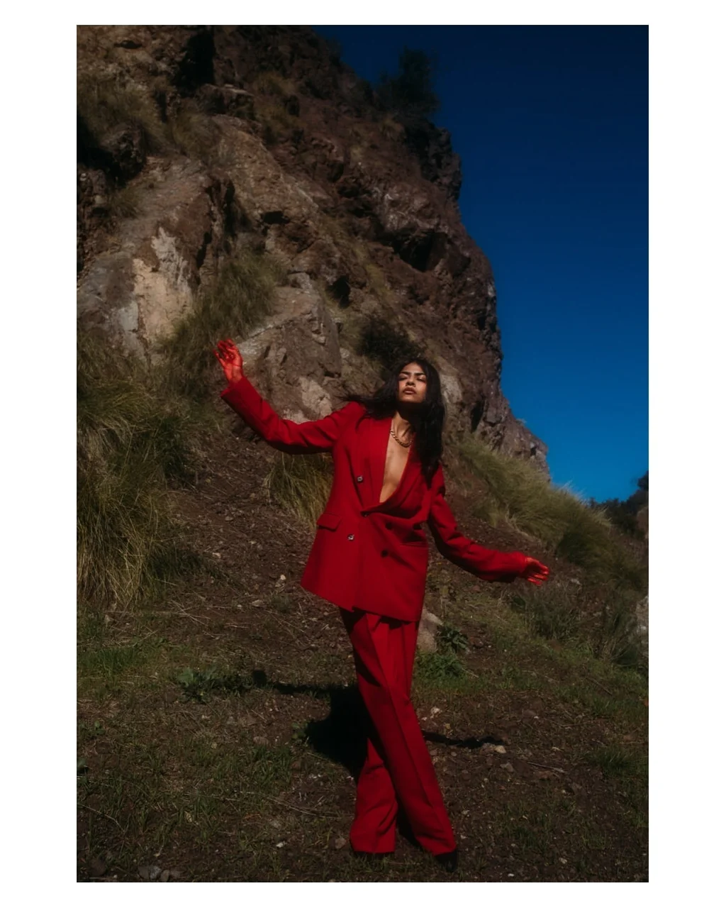 Figure in a red suit beneath a rocky hillside and blue sky