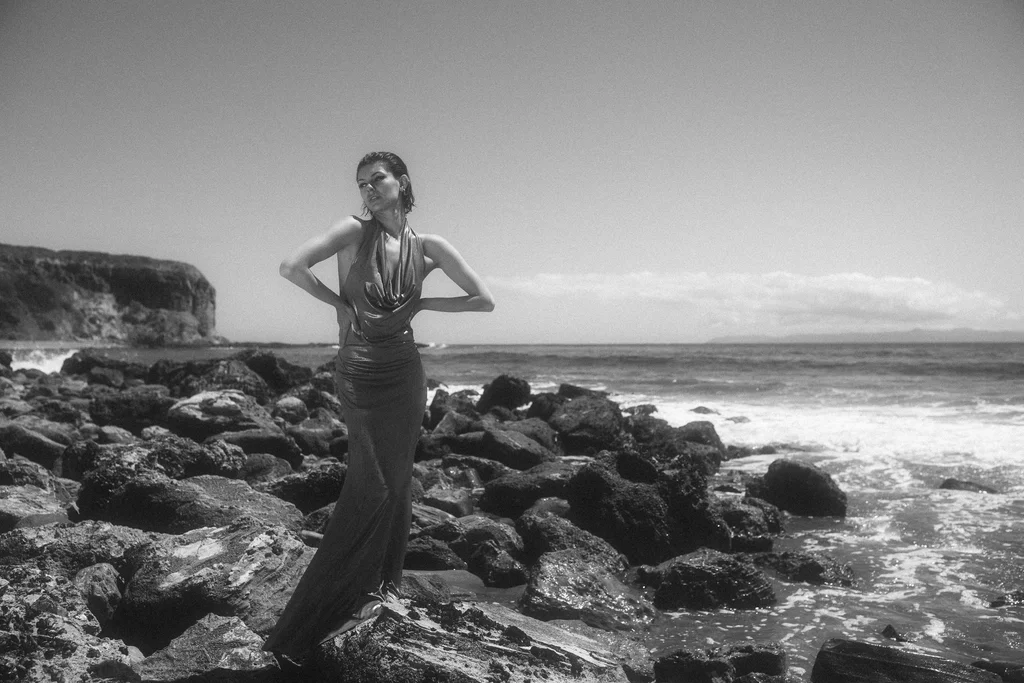 Black-and-white figure in a silver dress on a rocky coast