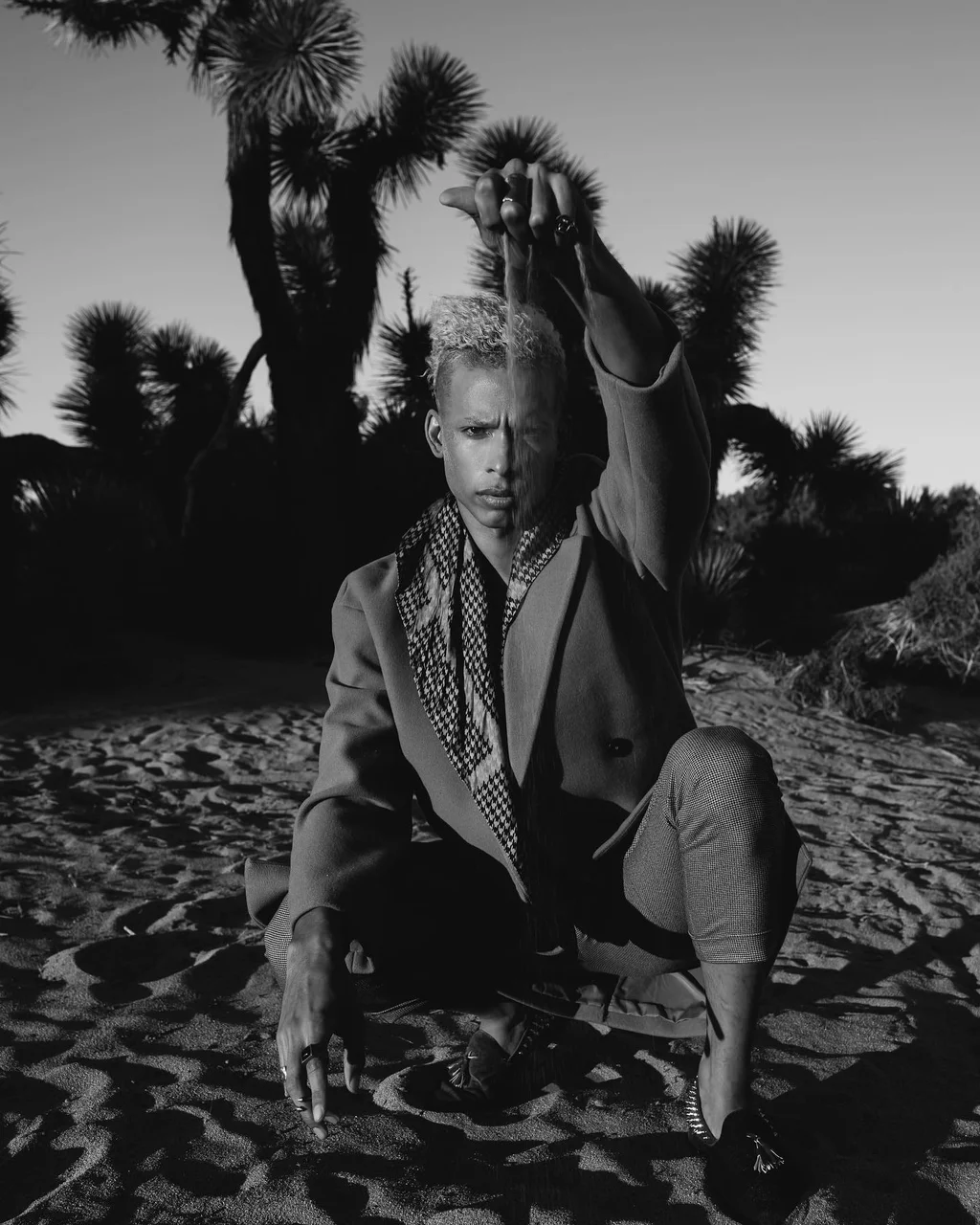 Black-and-white portrait in a tailored jacket beneath desert trees