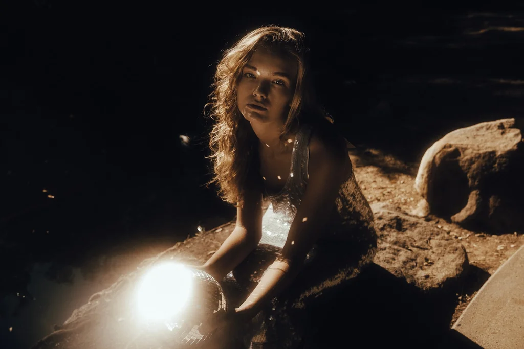 Figure in sequins beside a mirror ball on sunlit rocks