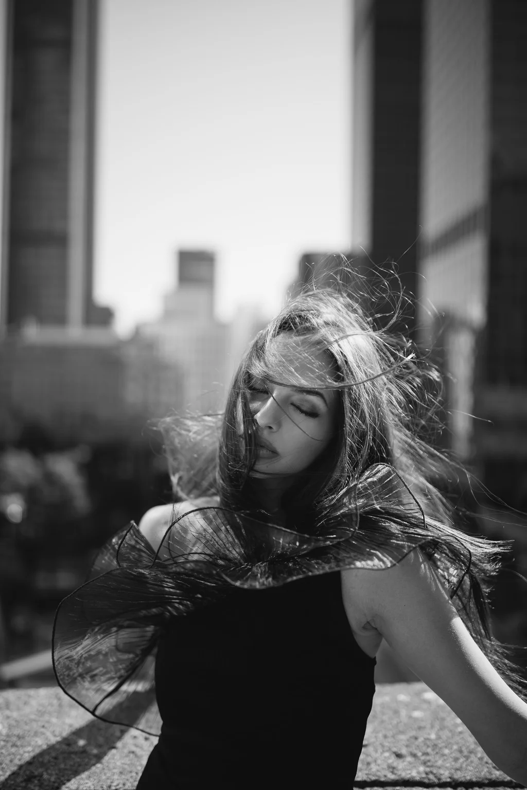 Windblown hair and sheer fabric against a monochrome skyline