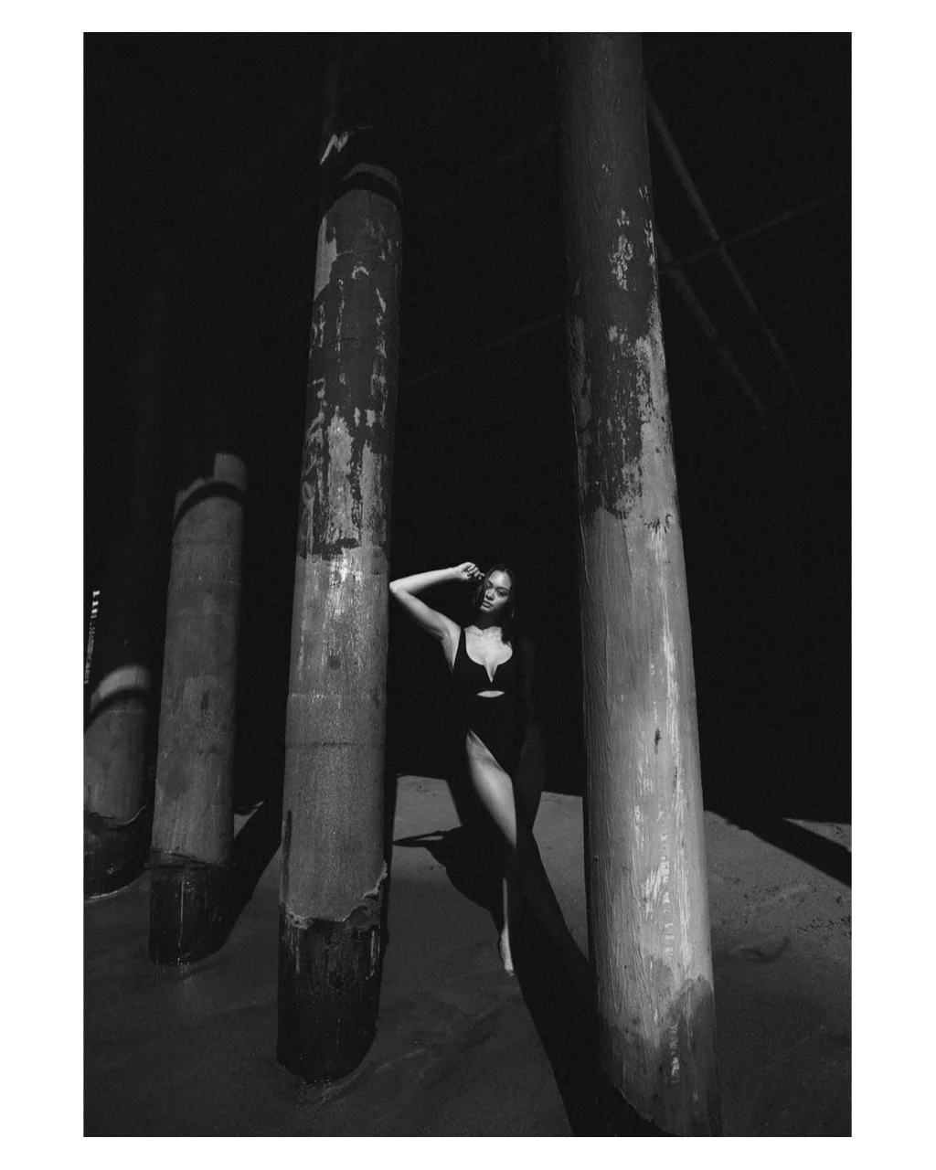 Black-and-white swimwear portrait between weathered pier columns