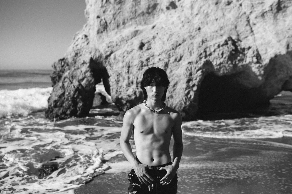 Black-and-white figure in the sea beneath a coastal rock arch