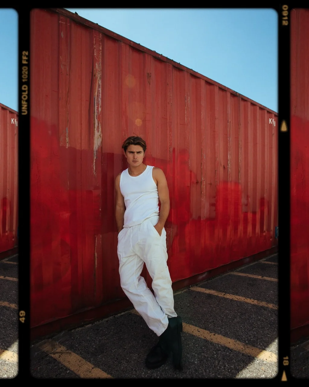 Figure in white beside a red shipping container, framed like a film negative