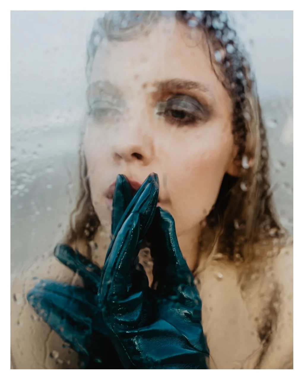 Beauty portrait through rain-speckled glass with blue gloves