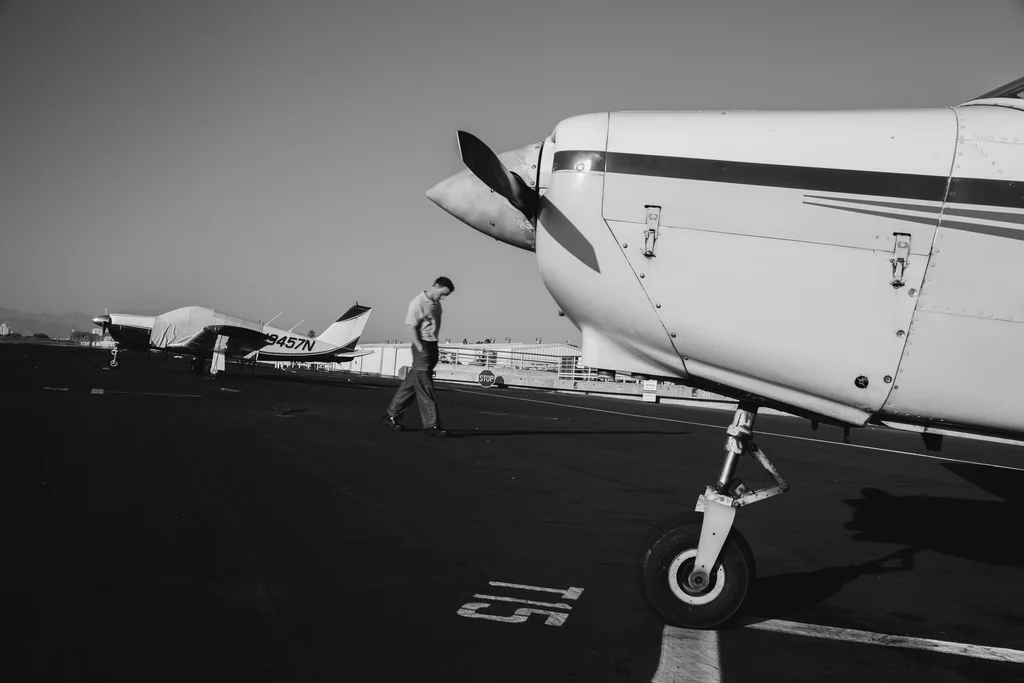 A wide black-and-white view across an airfield with a figure beside a plane