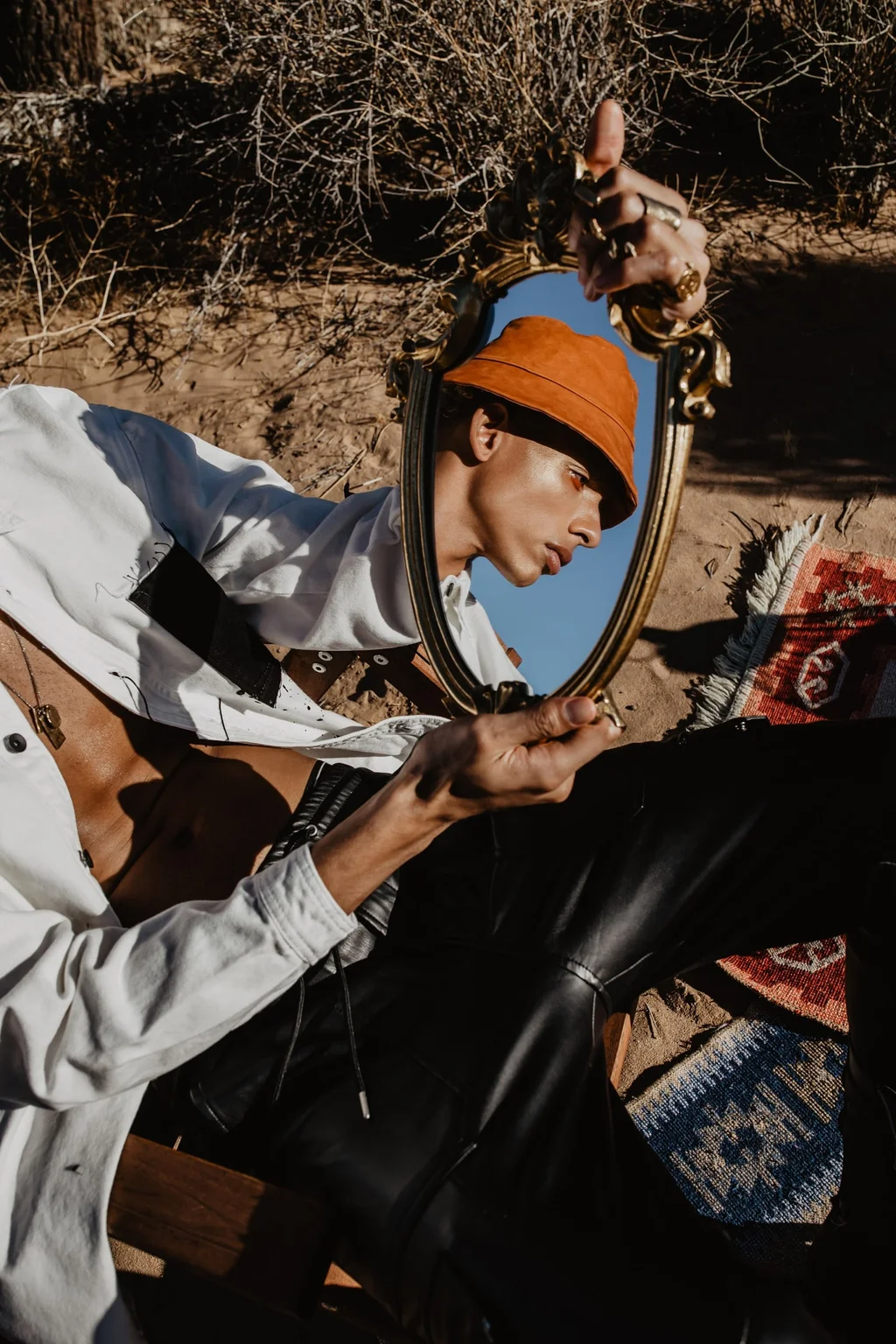 Figure in an orange hat with an ornate mirror on desert sand