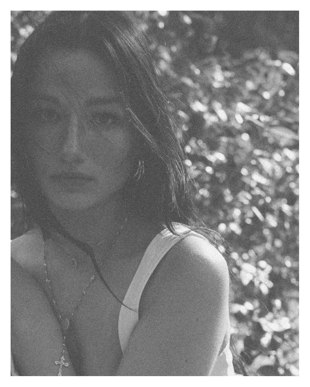 Grainy black-and-white portrait surrounded by sunlit leaves