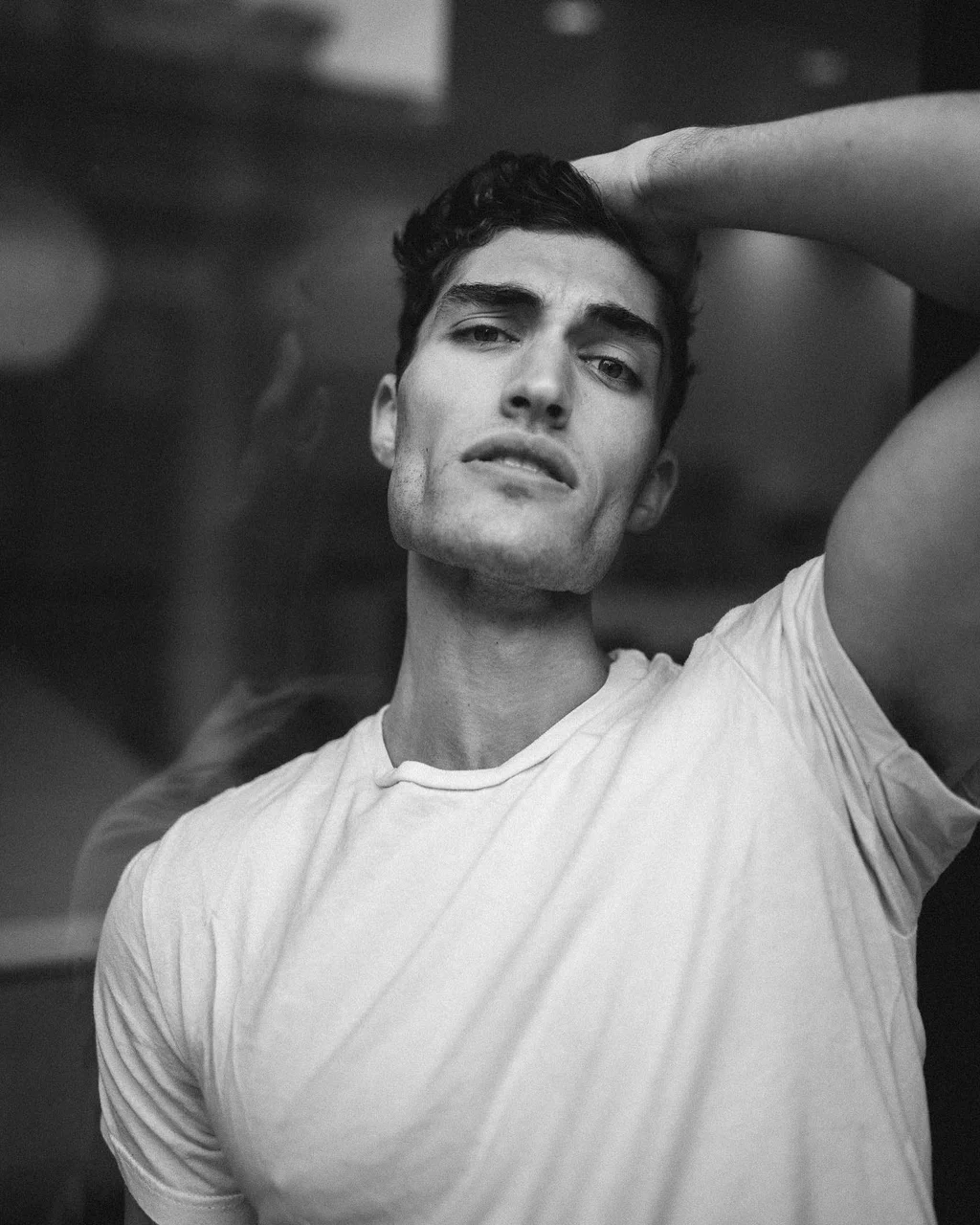 Black-and-white portrait in a white T-shirt with an arm raised overhead