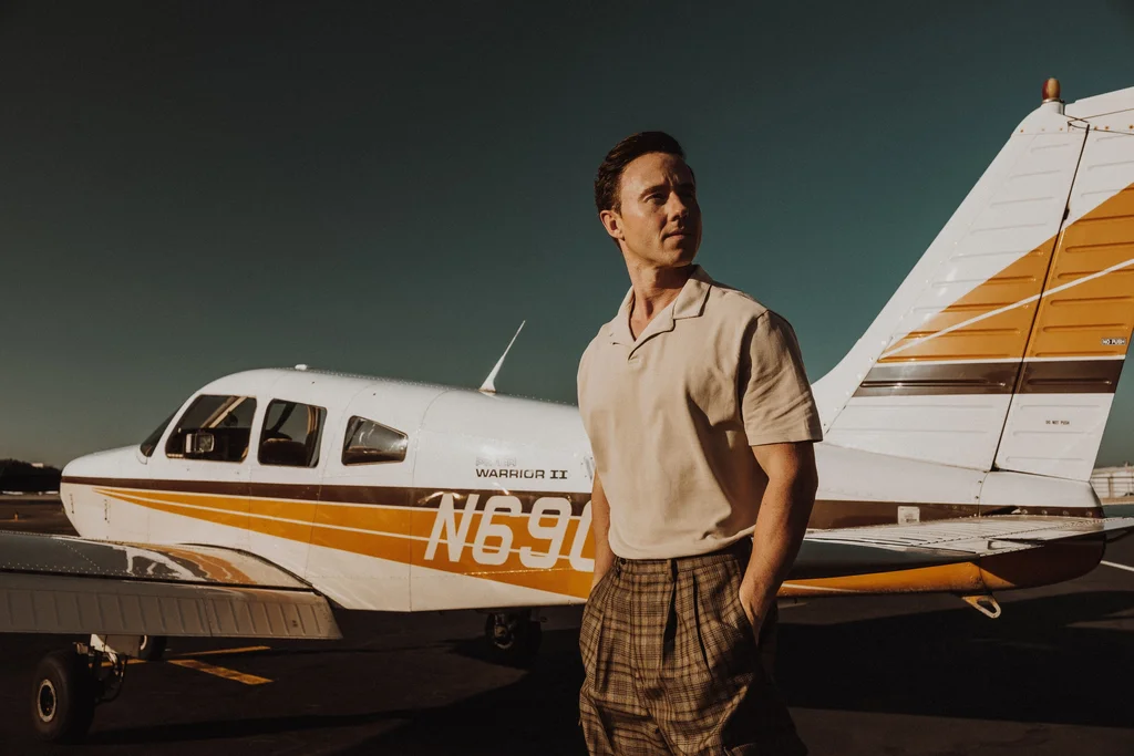 A figure in a pale shirt beside an orange-striped light aircraft