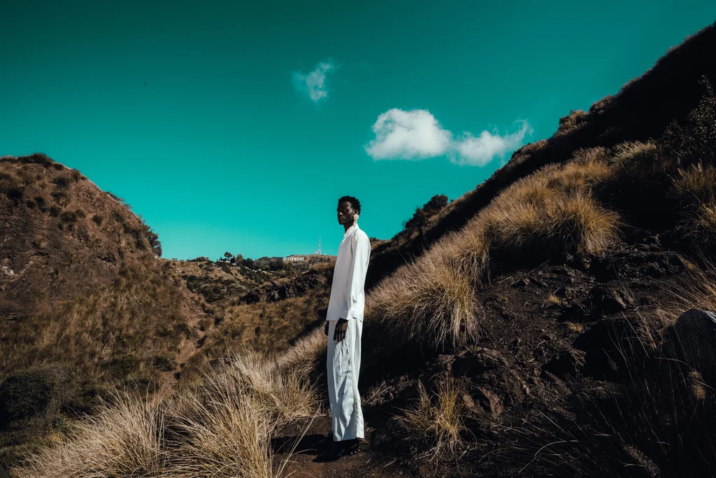 A figure in white between dry hills beneath a turquoise sky