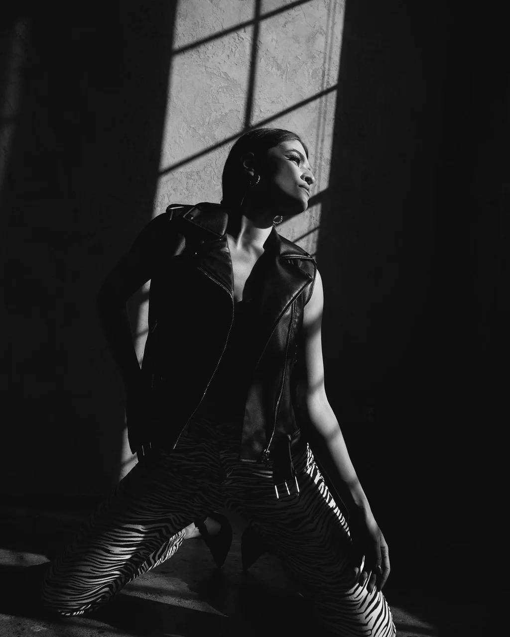 Black-and-white portrait in leather and zebra stripes under window shadows